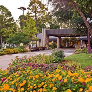 A beautifully landscaped area with vibrant flowers and lush trees surrounding a building entrance.