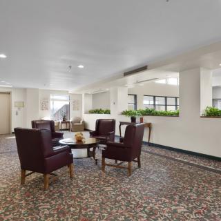 A spacious lobby seating area with chairs and a table, decorated with plants.