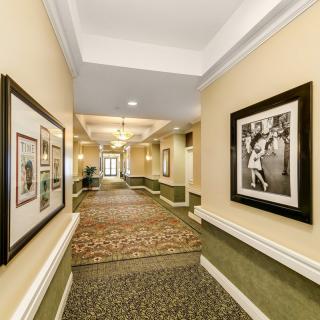 A well-lit hotel hallway adorned with framed artwork and a patterned carpet.