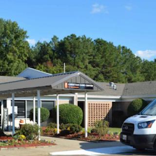A healthcare facility surrounded by greenery and a parked vehicle.