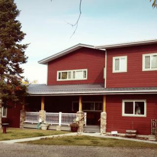 A two-story red house with a porch and surrounding greenery.