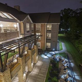 A nighttime view of a well-lit building with a pathway and surrounding trees.