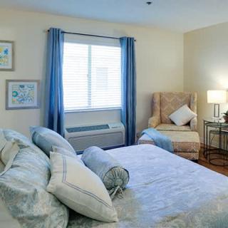 A cozy bedroom with a neatly made bed, a comfortable chair, and soft lighting.