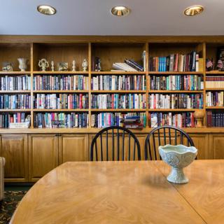 A cozy library with wooden bookshelves filled with books and a dining table in the foreground.