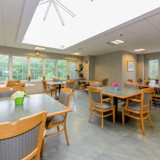 A bright and spacious dining area with multiple tables and chairs, featuring large windows that allow natural light to fill the room.