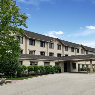 A three-story hotel building with an entrance and parking area surrounded by greenery.
