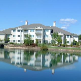 A large apartment building reflecting on a tranquil lake under a clear blue sky.