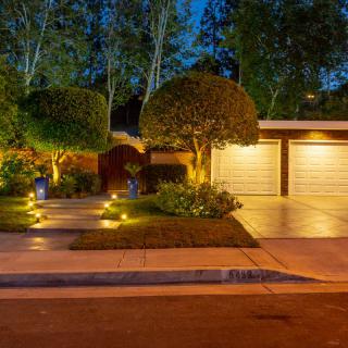 A well-lit house exterior and driveway with landscape lighting at night.