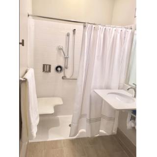 An accessible bathroom with a shower, sink, and a white curtain.