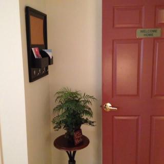 A red door next to a small table with a plant, and a wall-mounted bulletin board.