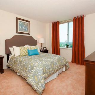 A well-decorated bedroom with a neatly made bed, warm-colored curtains, and a window view.