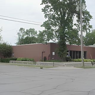 A brick building with a parking lot and surrounded by trees.