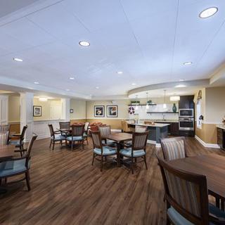 A spacious dining area with tables and chairs, featuring a kitchen in the background and wooden flooring.