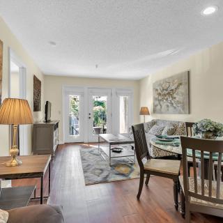 A cozy living room with wooden flooring, featuring a sofa, coffee table, and dining area.