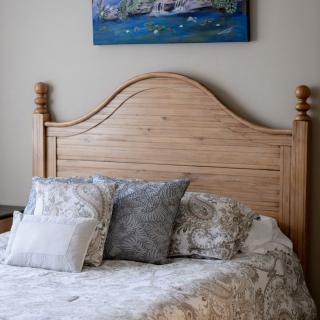 A cozy bedroom with a wooden headboard, decorative pillows, and a painting on the wall.