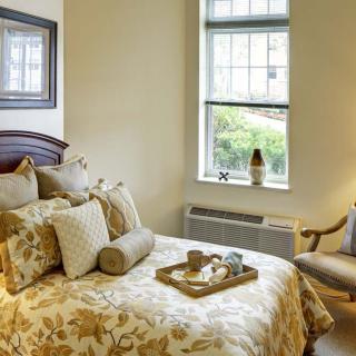 A cozy bedroom with a nicely decorated bed, featuring plush pillows and a tray. A window allows natural light to enter, complementing the warm interior design.