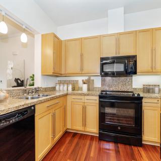 A modern kitchen with light wood cabinets, granite countertops, and black appliances.