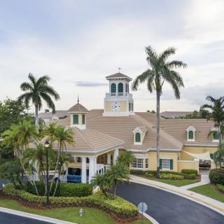 A tropical-style building surrounded by palm trees with a driveway in front.