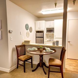 A cozy dining area with a small round table and two chairs, adjacent to a modern kitchen in an apartment.