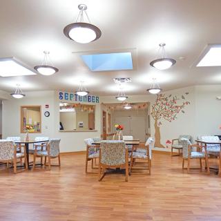 A spacious dining room with multiple tables and chairs, featuring decorative lighting and a wooden floor.
