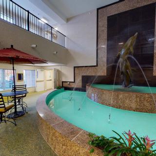 An indoor setting featuring a decorative fountain, seating area with an umbrella, and surrounding plants.