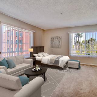 A spacious bedroom with a cozy seating area, featuring a bed and sofa near large windows that let in ample natural light.