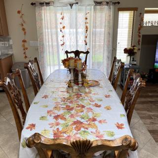 A dining room with an autumn-themed table setting, featuring a decorated tablecloth and chairs.