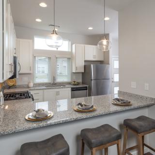 A modern kitchen with a granite countertop, bar stools, and stainless steel appliances.