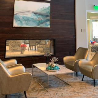 A modern lounge area featuring comfortable chairs, a central table, abstract artwork, and a sleek fireplace.