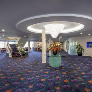 A spacious lobby area with a modern chandelier, vibrant carpet, and a central staircase.