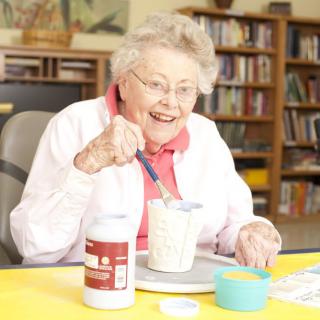 An elderly woman enjoying a crafting activity indoors, surrounded by art supplies.