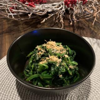 A bowl of fresh spinach garnished with a topping, placed on a textured mat.
