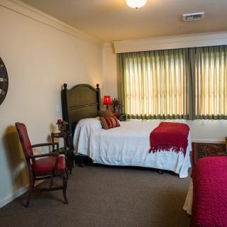 A cozy bedroom with twin beds featuring red and white bedding, a decorative clock on the wall, and a comfortable chair beside the window.