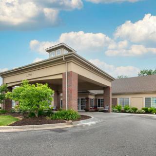 A modern building with an entrance canopy and landscaped surroundings under a partly cloudy sky.