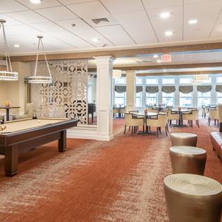 A modern recreation room featuring a shuffleboard table and ample seating.