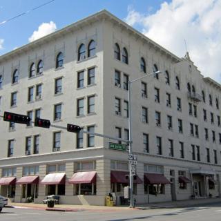 A historic multi-story building located at a street corner, featuring numerous windows and awnings.