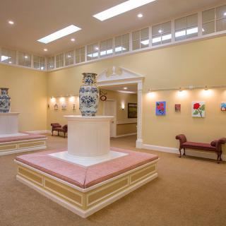 A well-lit art gallery interior featuring sculptures and colorful paintings on display.