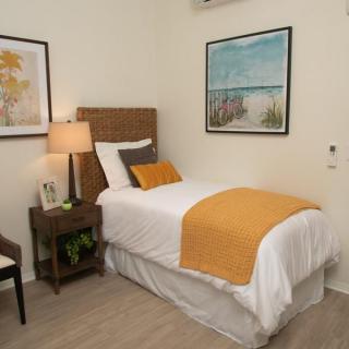 A cozy bedroom with a single bed adorned with orange accents, complemented by tasteful artwork and a warm lamp.
