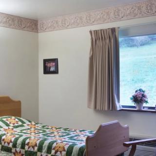 A cozy bedroom with a single bed, patterned quilt, and a window with curtains overlooking greenery.