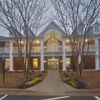 A symmetrical building with large windows and an inviting entrance, flanked by trees and illuminated by glowing lights.