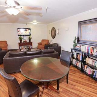 A cozy living room featuring a leather sofa set, a round wooden table with chairs, a television, and a bookshelf filled with books.