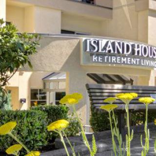 Entrance to Island House Retirement Living surrounded by yellow flowers and greenery.