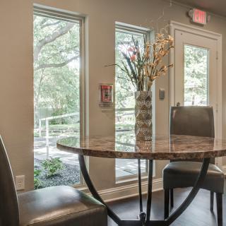 A cozy dining area with a round table and chairs, illuminated by natural light from large windows.