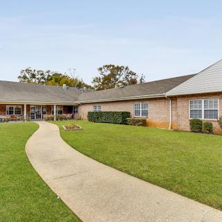 An exterior view of a building with a pathway leading through a well-manicured lawn, surrounded by trees.