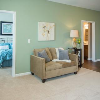 A cozy living area with a beige sofa, green walls, and a view into the bedroom and bathroom.