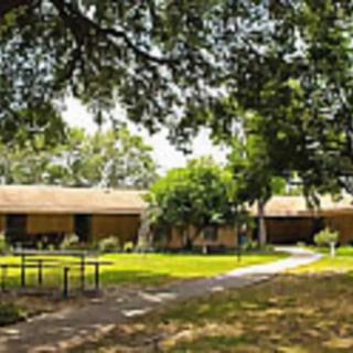A single-story building surrounded by trees and a well-maintained yard with a pathway leading to the entrance.