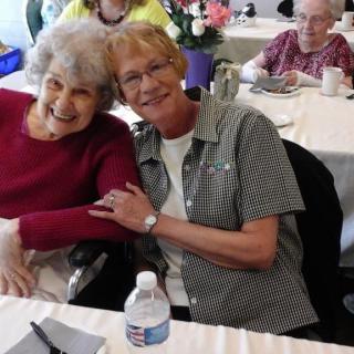 Two women smiling and embracing at a social gathering indoors.
