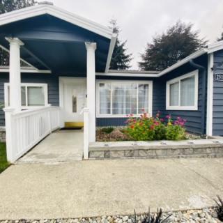 A welcoming blue house with a front porch and ramp, surrounded by a small garden.