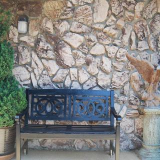An outdoor bench against a stone wall with potted plants.