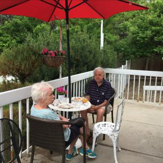 An elderly couple enjoying a conversation on a patio under a red umbrella.